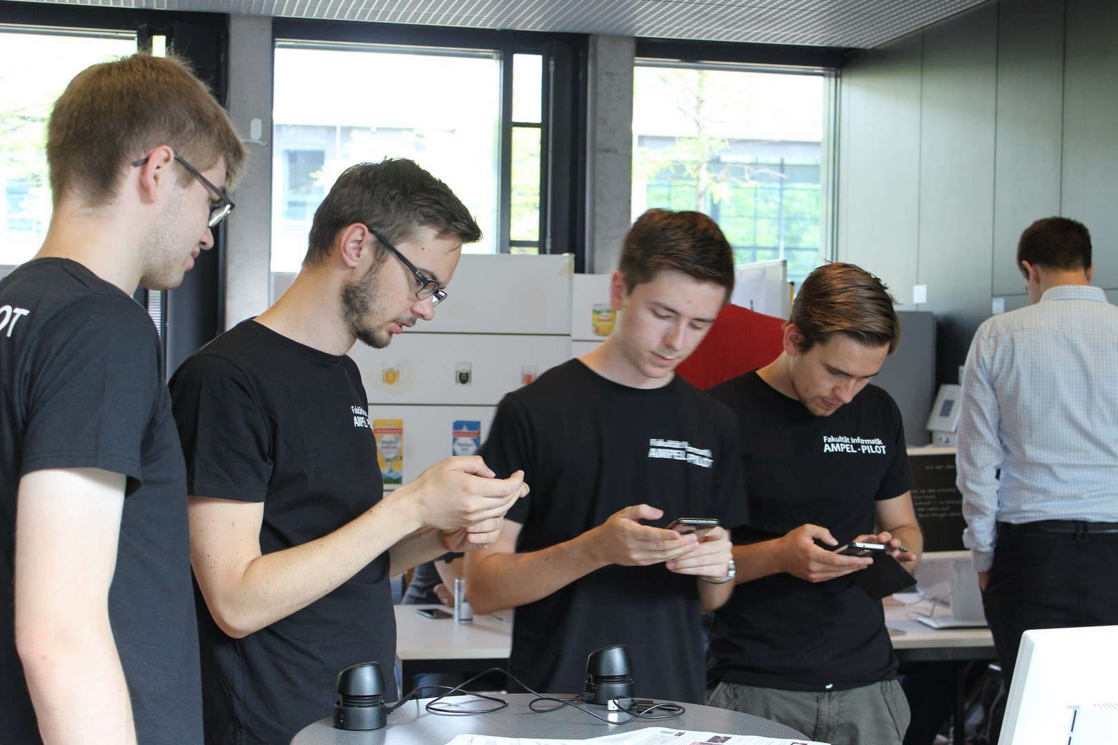Foto des Projekttags: Vier Studenten des Projektteams stehen nebeneinander und sehen auf ihre Mobiltelefone